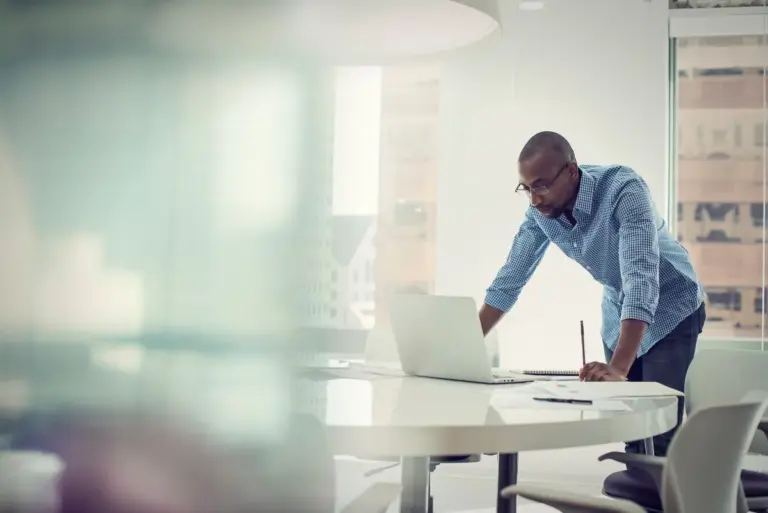 Executive in office leaning over laptop